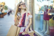 A woman shops in the city while holding her phone and a credit card.