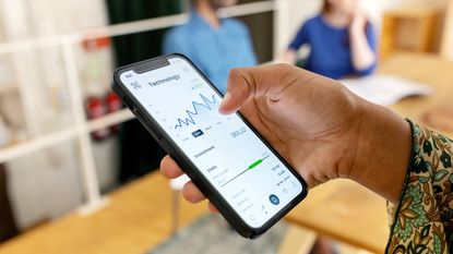 A woman holds a smartphone that shows a graphic tracking stock trading.