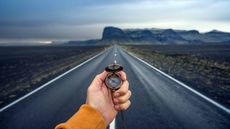 person holding compass standing on empty highway looking toward mountains