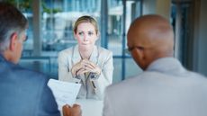 A young woman looks nervous as she sits across the table from two men who are interviewing her for a job.