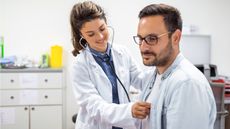 A doctor uses her stethoscope to listen to a man's heart in a doctor's office.