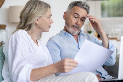 A mature couple doing paperwork with a laptop at home. They look concerned about finances.