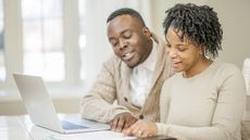 A couple look happy as they look over financial paperwork at the kitchen table.