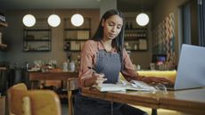 A small business owner looks over paperwork while sitting at a table in her shop.