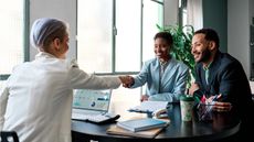 A tax adviser shakes hands across her desk with a client couple.