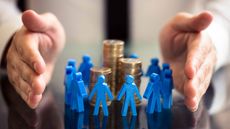 man shielding tiny blue figurines circling stacks of coins