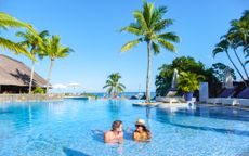 A couple relaxes in a luxury hotel pool with a view of the ocean behind them.