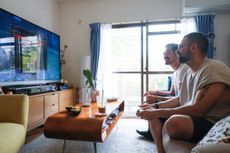 Two men sitting on the living room couch watching TV 