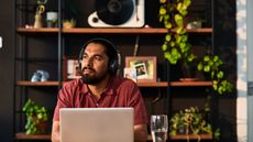 A man wearing headphones looks like he's considering something while sitting at his desk.