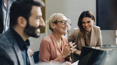 Three office workers smile and laugh during a meeting in a conference room.